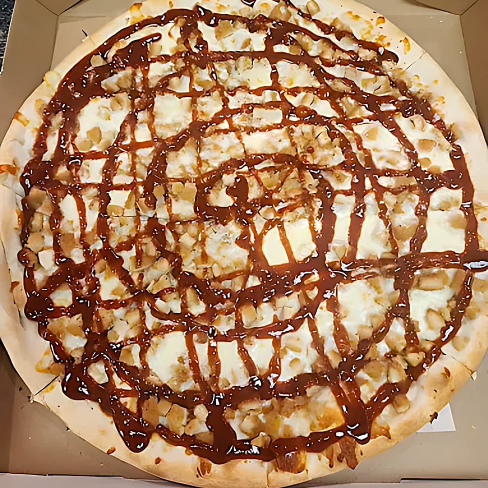 A Tuscana Pizza & Pasta dessert pizza with white frosting, nuts, and a chocolate drizzle.