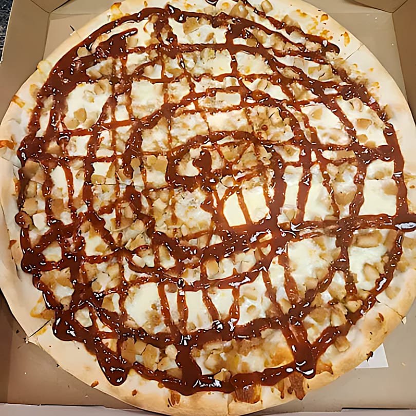 A Tuscana Pizza & Pasta dessert pizza with white frosting, nuts, and a chocolate drizzle.