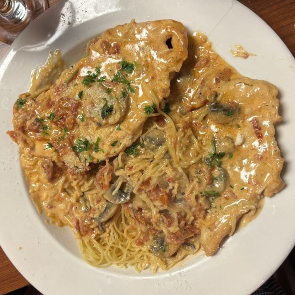 Chicken and pasta dish with creamy sauce, mushrooms, and parsley on a white plate.