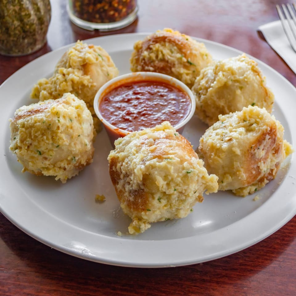 Six Tuscana garlic knots with parmesan cheese and herbs, served with a side of marinara sauce.