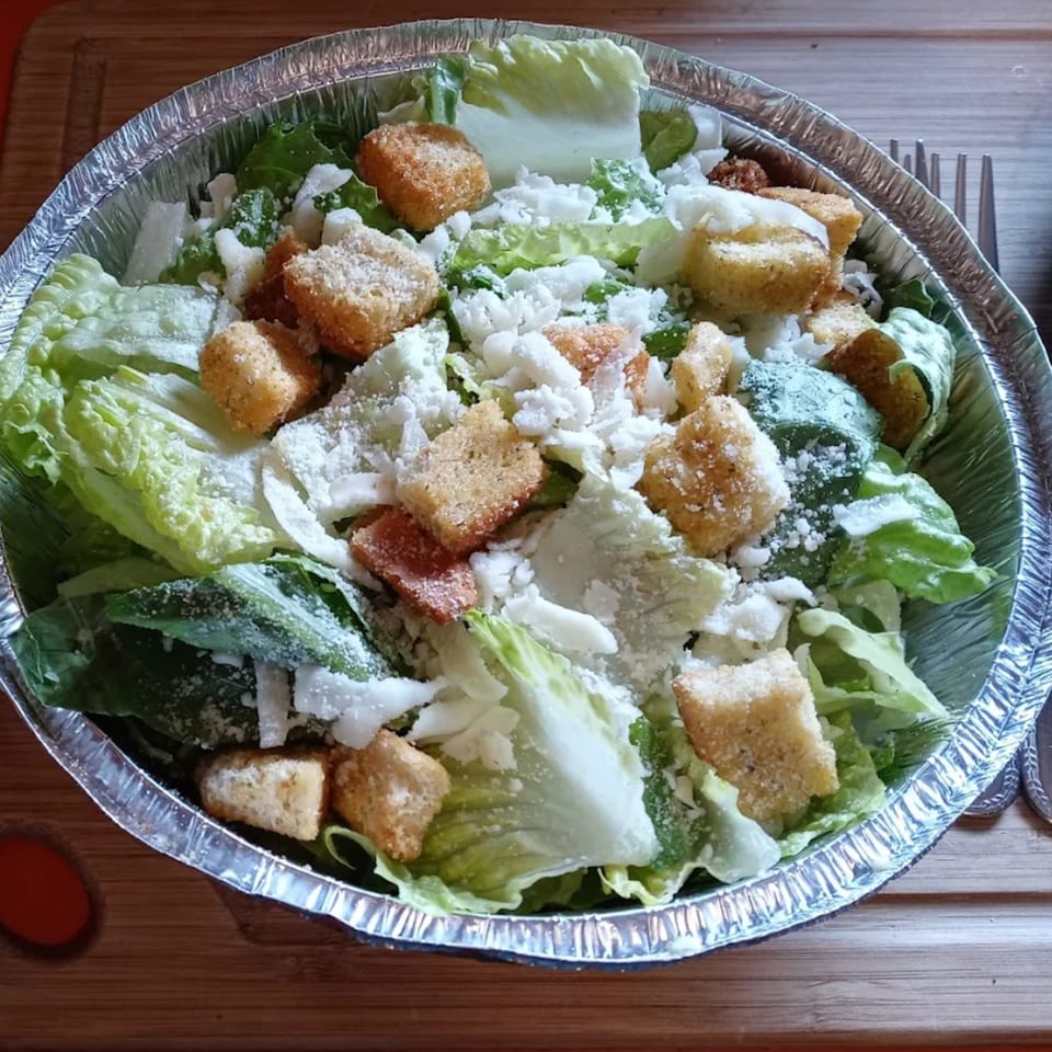 Caesar salad with romaine lettuce, croutons, and parmesan cheese in a foil container.