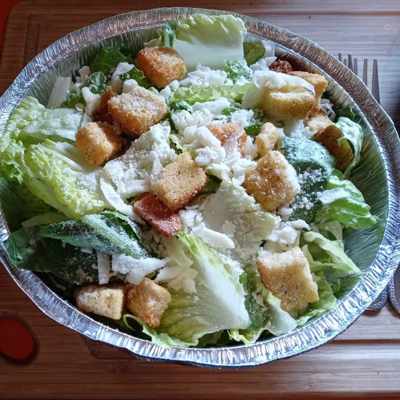 Caesar salad with romaine lettuce, croutons, and parmesan cheese in a foil container.