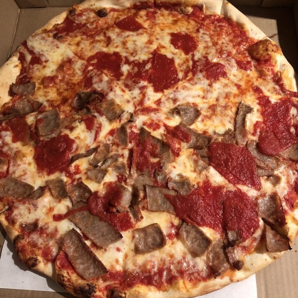 A whole Tuscana Pizza & Pasta pizza with sausage and red sauce in a cardboard box.