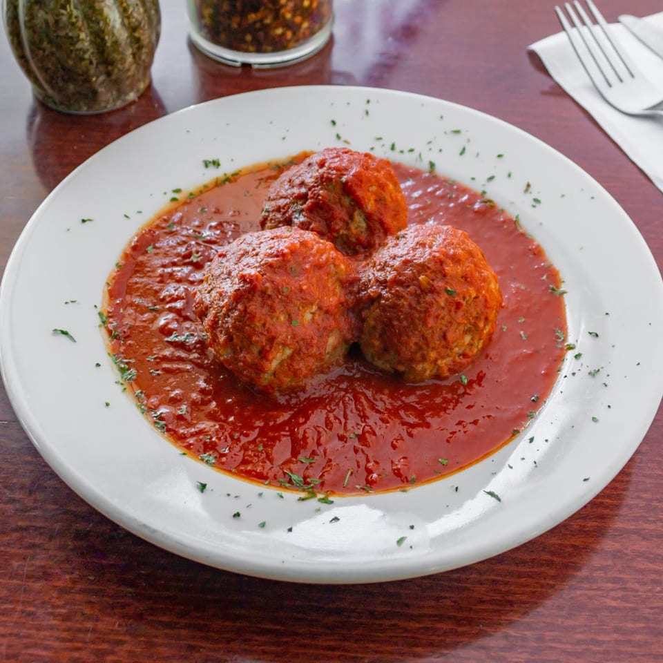 Three large meatballs covered in red marinara sauce and sprinkled with herbs on a white plate.